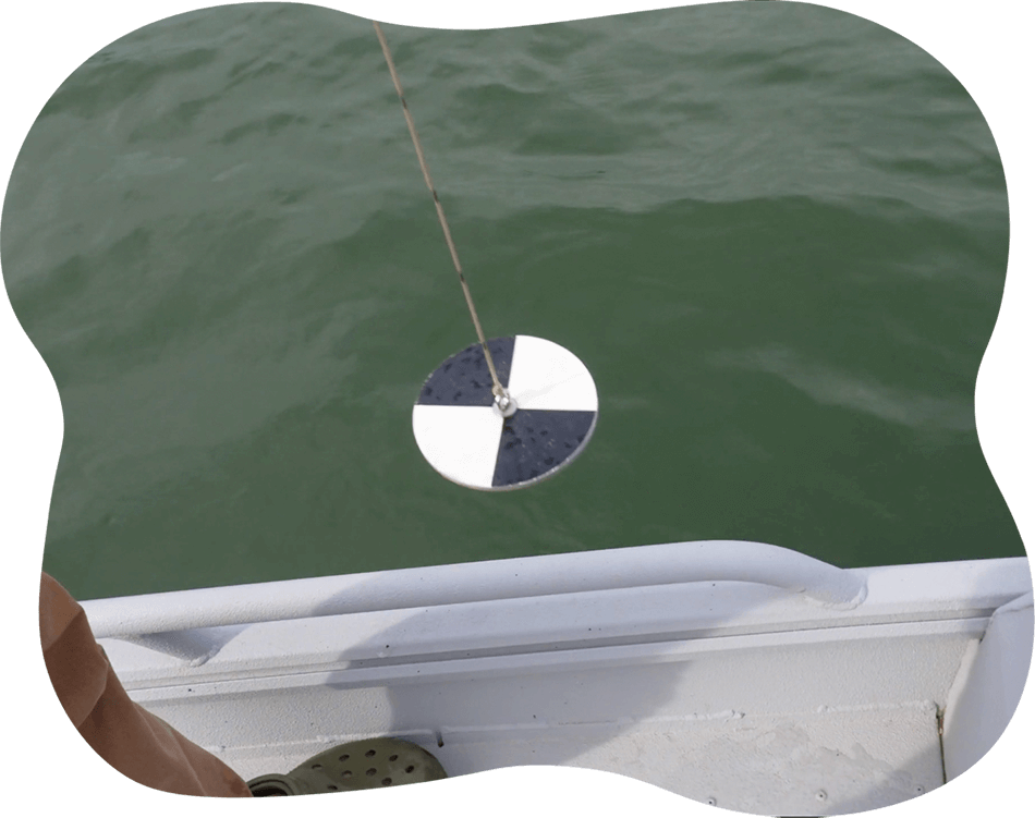Black and white round disk being lowered from a boat into lake water